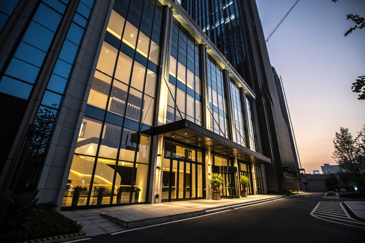 Modern commercial office building exterior at sunset with glass facade and warm interior lighting.